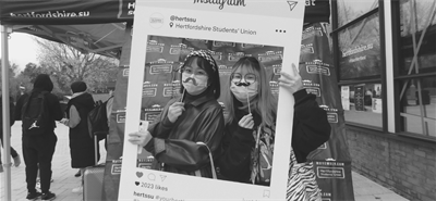 Two people with masks on holding up moustaches and an instagram frame