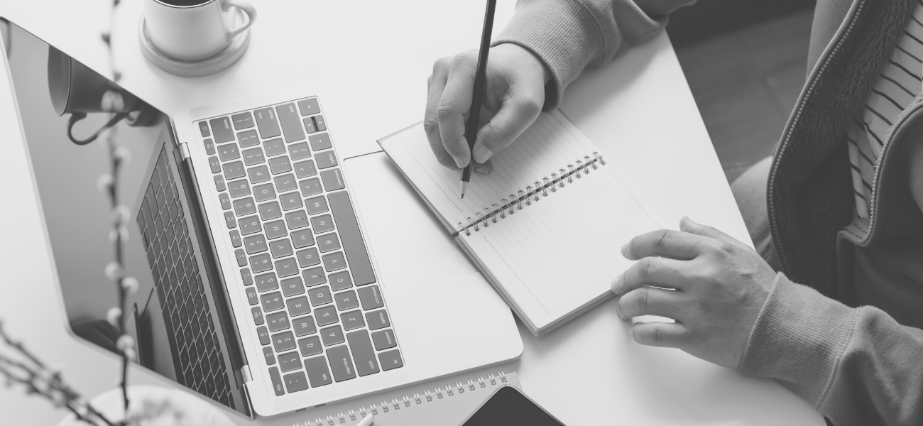 Person writing in a notebook in front of a laptop